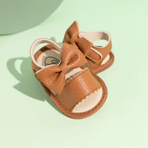 Close-up of brown PU baby sandals with bow decoration and serrated lace edges