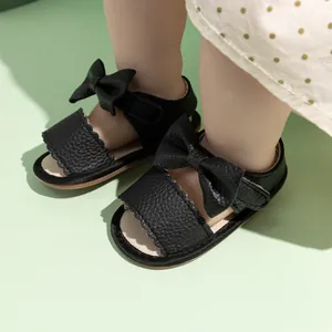 Detailed view of black PU leather baby sandals featuring a large bow and wavy trim