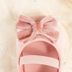 Détail de chaussures bébé en velours rose avec double nœud sur fond de dentelle
