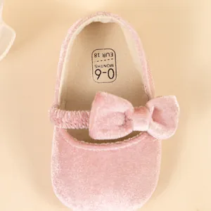 Détail de chaussures bébé en velours rose avec nœud et étiquette de taille 0-6 mois