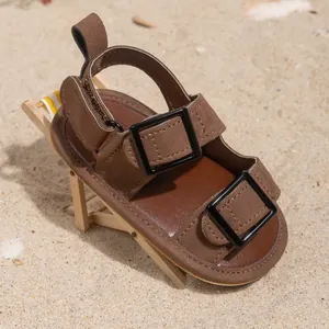 Brown faux suede baby sandals with dual buckles on a miniature beach chair