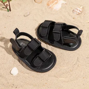 Fashionable black baby sandals with buckle design on a summer beach background