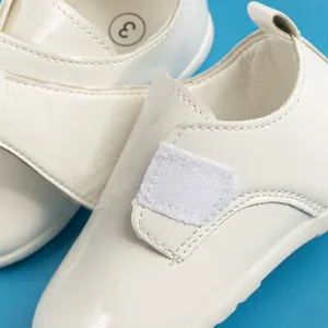 Dettaglio macro di scarpe per neonati in pelle verniciata bianca con velcro su sfondo blu