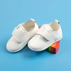 Dettaglio di scarpine da neonato in vernice bianca con chiusura a strappo blu