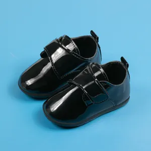 Dettaglio di scarpe per neonati in pelle verniciata nera con chiusura a strappo