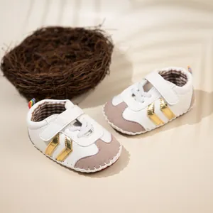 Infant walking sneakers with gold stripes and velcro closure on warm beige background
