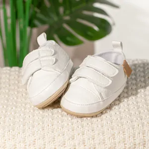 Close-up of white leather baby shoes with velcro straps on cozy knit background
