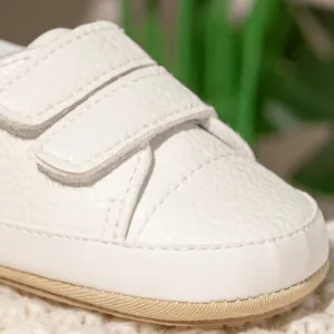 Close-up of white leather baby walking shoes with dual hook-and-loop straps and textured sole