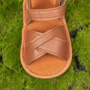 Detailed macro view of brown pebbled leather texture on baby sandals with cross straps