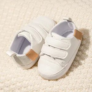 Detail of white leather baby walking shoes with triple velcro straps on knit background
