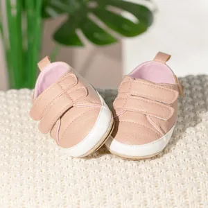 Pink faux leather baby walking shoes with anti-slip rubber soles on white knit rug