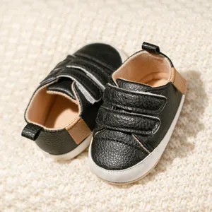 Black leather baby walking shoes with triple Velcro straps on a cozy knit background