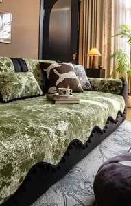 Detail of dark green chenille sofa cover with white floral pattern and black pompom fringe