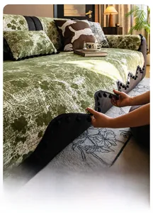 Detail of green chenille sofa cover with black pom-pom fringe and anti-wrinkle texture