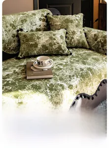 Close-up of green chenille sofa cover with black pom-pom edges and marble texture