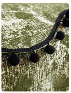 Detail of chenille sofa cover showing green white jacquard texture and black pompom fringe