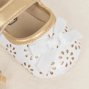 Macro view of white Mary Jane baby shoes with floral cutouts and gold lining trim