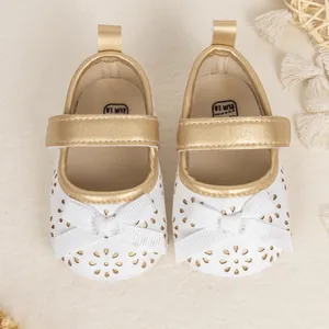 Close-up of white baby Mary Jane shoes with laser-cut flowers and gold trim details