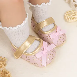 Detailed view of pink baby Mary Jane shoes with floral cut-outs and bow on white carpet
