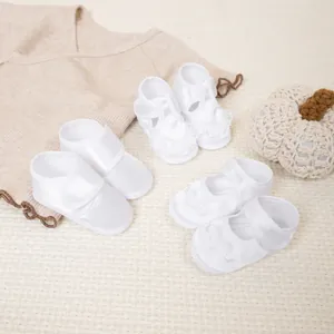 Trois modèles de chaussures bébé en satin blanc à semelles souples et détails en dentelle