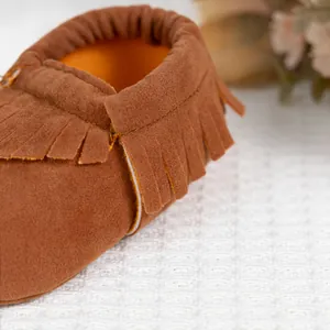 Détail de mocassins pour bébé marron avec franges, texture en daim et ouverture élastique