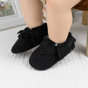 Détail de chaussures bébé en daim noir avec franges sur tapis gaufré blanc