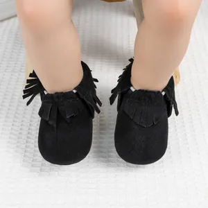 Gros plan de mocassins pour bébé en daim noir avec franges sur fond de tricot blanc