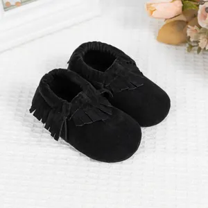 Gros plan de mocassins pour bébé noirs à franges sur un tissu gaufré blanc doux
