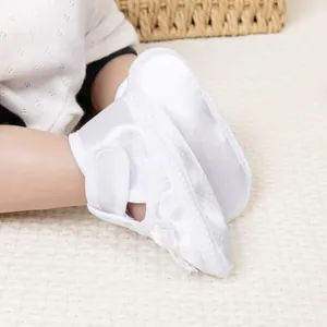 Gros plan de chaussures bébé en satin blanc avec scratch sur texture tissée