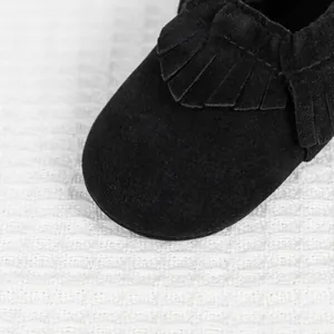 Gros plan détaillé des franges en daim noir et de la texture douce du chausson pour bébé