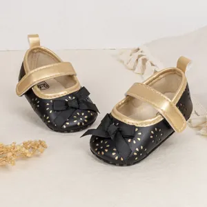 Close-up of baby Mary Jane shoes with laser-cut flower patterns and gold trim bow