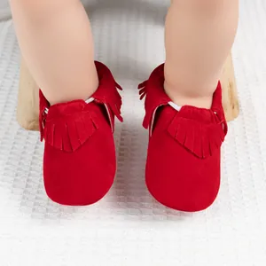 Détail de chaussures bébé rouges à franges avec semelle souple sur un tapis blanc