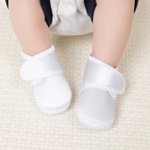 Détail de chaussures de baptême en satin blanc à semelle souple et fermeture velcro
