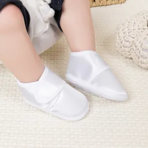 Détail de chaussures de baptême pour bébé en satin blanc avec fermeture velcro pratique