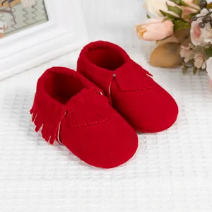 Mocassins pour bébé en daim rouge avec franges et semelles souples sur fond blanc