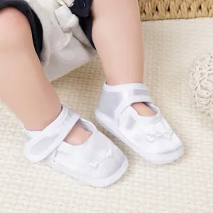 Gros plan de chaussures bébé en satin blanc avec broderie cœur et bride à scratch