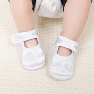 Détail de chaussures bébé en satin blanc avec broderie cœur délicate et bride velcro