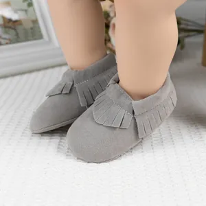 Détail de mocassins gris clair pour bébé avec franges et semelle souple sur tapis