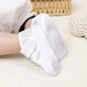 Vue détaillée des chaussures bébé en satin blanc avec fermeture velcro sur tapis tissé