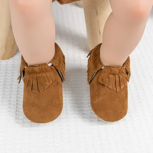Gros plan de mocassins pour bébé en daim marron avec franges sur tapis blanc doux