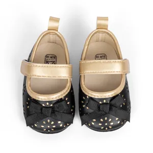 Top view of baby Mary Jane shoes with black floral cutouts and gold bow detail