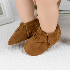 Gros plan de bottines pour bébé en daim marron foncé avec franges sur un tapis texturé