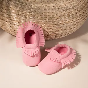 Détail de bottines pour bébé en daim rose avec glands décoratifs et semelle souple élastique