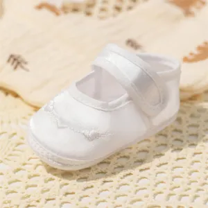 Détail de chaussures de baptême en satin blanc avec broderie et ruban velcro