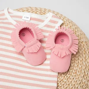 Détail de bottines bébé à franges roses et tenue rayée sur fond de tapis tressé