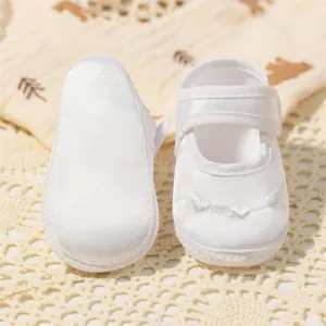 Détail de chaussures de baptême en satin blanc pour bébé avec broderie cœur