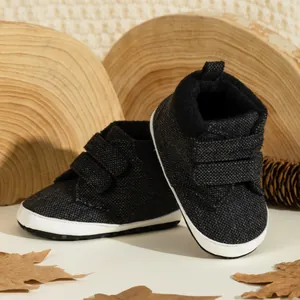Dark grey infant soft sole walking shoes with velcro straps on a wooden tray