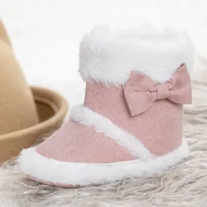 Detail of pink baby snow boot with bow and plush faux fur lining on a soft rug