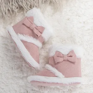 Detail of pink baby winter boots with soft faux fur trim and bow on plush background