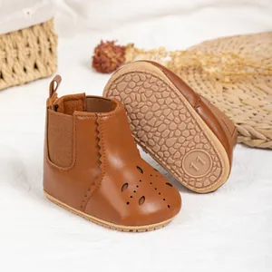 Detail showing non-slip rubber soles and hollow-out floral pattern on brown baby boots